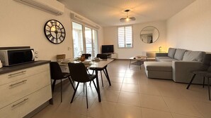 Een moderne woonkamer met een eethoek, een grijze bank, een flatscreen televisie en een grote wandklok.