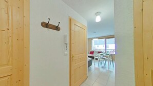 A hallway with wooden doors, a coat rack, and a view into a dining area with a table and chairs. - Cozy apartment with mountain view - 4 guests (Le Grand-Bornand)