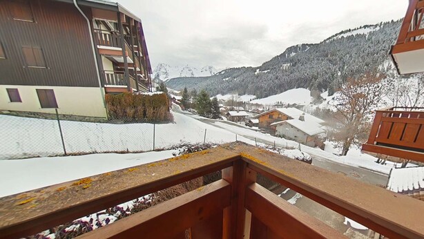 A balcony with a view of a snow-covered village and mountains. - Cozy apartment with mountain view - 4 guests (Le Grand-Bornand)