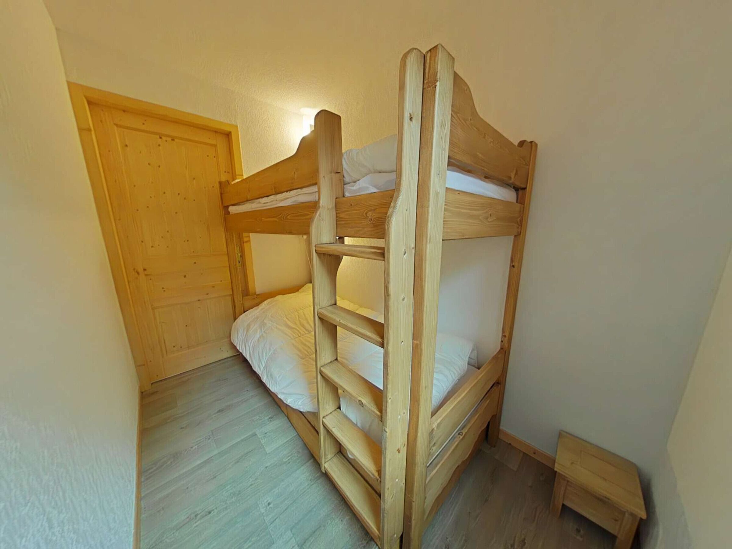 Un lit superposé avec une tête de lit en bois et une petite table de chevet en bois à côté.