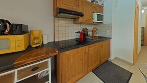 A compact kitchen with wooden cabinets, a microwave, a coffee maker, and a toaster. - Cozy apartment with mountain view - 4 guests (Le Grand-Bornand)