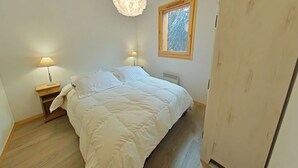 A bedroom with a bed, bedside lamps, a window, and a wardrobe. - Cozy apartment with mountain view - 4 guests (Le Grand-Bornand)