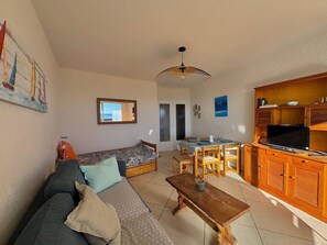 A cozy living room with a sofa, a wooden bench, and a dining area with a table and chairs. - Seafront apartment with terrace and parking (Le Lavandou)