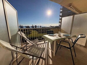 Un balcón con una mesa y sillas, vista al mar y cielo despejado.