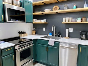 Une cuisine moderne avec des armoires de couleur turquoise, des appareils électroménagers en acier inoxydable et des étagères en bois.