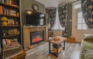 Ein gemütliches Wohnzimmer mit Kamin, Fernseher und einer Bücherwand voller Bücher.