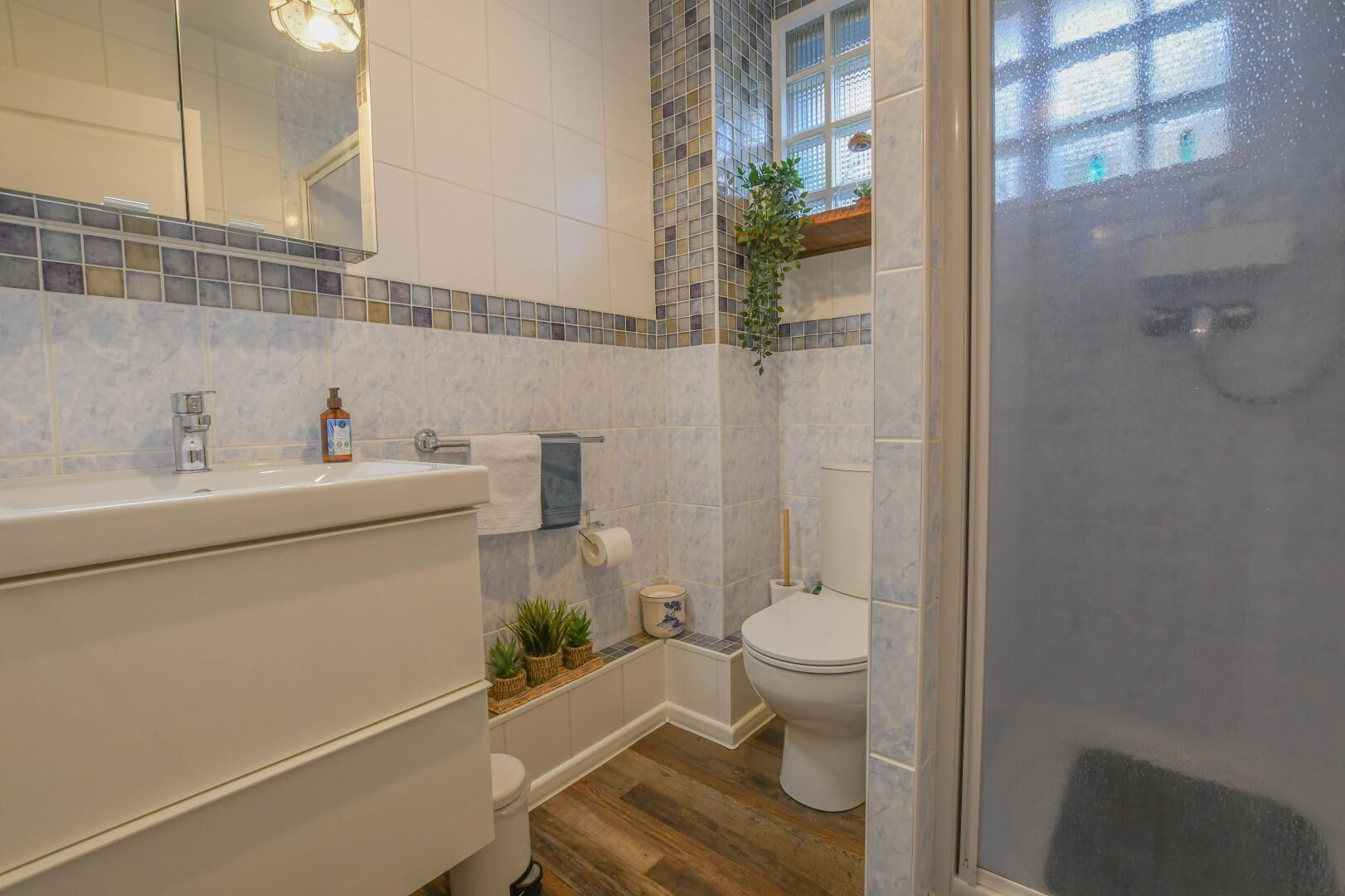 Ein Badezimmer mit Waschbecken, Toilette und Dusche. Über dem Waschbecken befindet sich ein Spiegel, über der Toilette ein Fenster.