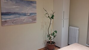 A bedroom with a bed, a radiator, a wardrobe, a potted plant, and a painting of a sailboat on the wall. - Cozy apartment in lovely and peaceful part of Belgrade (Belgrade)