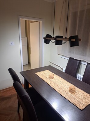 A dining area with a dark wooden table, two chairs, a woven placemat, and a pendant light fixture. - Cozy apartment in lovely and peaceful part of Belgrade (Belgrade)