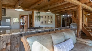 Un intérieur rustique avec un plafond en bois, un îlot de cuisine, un canapé et un escalier.