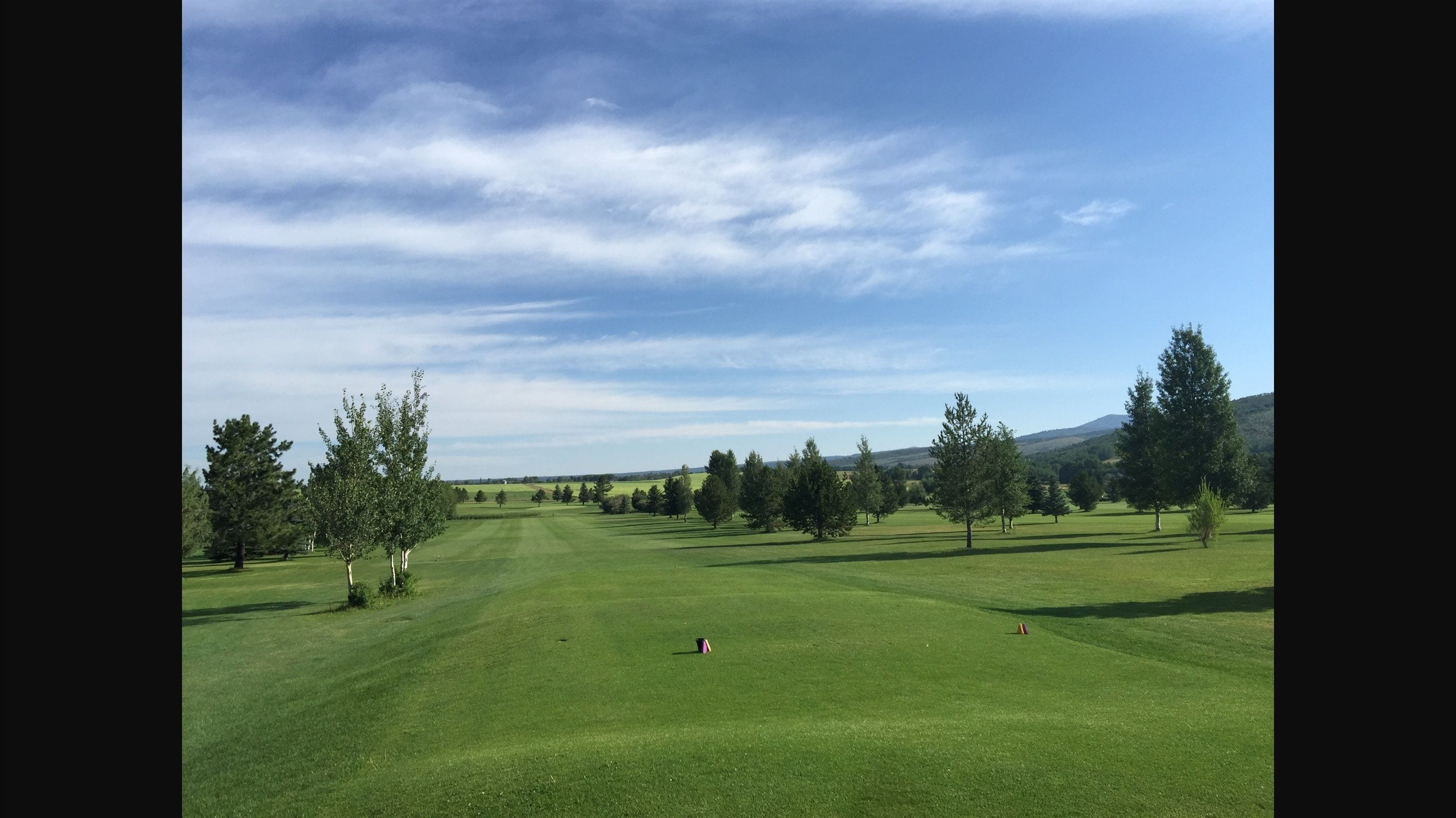 Un parcours de golf avec un ciel dégagé, des arbres et des collines à l’horizon.