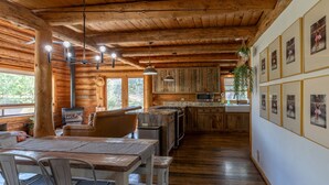 L’intérieur d’un chalet rustique comprend une table à manger en bois, des chaises, un coin cuisine et des tableaux encadrés accrochés aux murs.