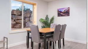 Ein Essbereich mit einem Holztisch und vier Stühlen, einem Fenster mit Blick auf Felsen und einem Bild an der Wand.