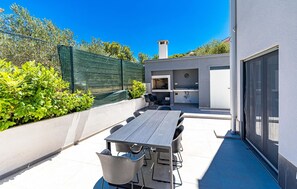 Une terrasse extérieure avec une table et des chaises, un barbecue et une porte-fenêtre coulissante.