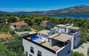 Un quartier résidentiel moderne composé de plusieurs immeubles, dont une maison dotée d’une piscine sur le toit et de panneaux solaires.