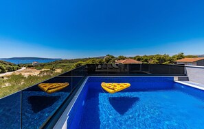 Une piscine à débordement située sur le toit, avec une eau d’un bleu cristallin, et offrant une vue panoramique sur la mer et les collines environnantes.