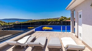 Una piscina en la azotea con agua cristalina, rodeada de sillones de descanso y una barandilla de vidrio.