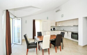 Una cocina moderna con armarios blancos, una mesa de comedor con sillas y un puerta corrediza de vidrio que da a un balcón.