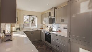 A modern kitchen with stainless steel appliances, white cabinetry, and a herringbone floor pattern. - Hunters Cottage – A Romantic Luxury Retreat with Hot Tub & Slipper Bath, AC (Blandford Forum)