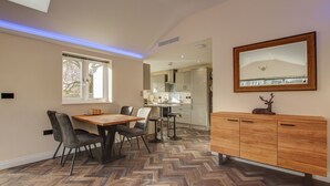 A modern kitchen with a herringbone floor pattern, a dining area with a wooden table and chairs, and a wooden cabinet with a deer decoration. - Hunters Cottage – A Romantic Luxury Retreat with Hot Tub & Slipper Bath, AC (Blandford Forum)