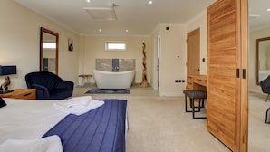 A modern bedroom with a large bed, a sitting area with a chair, a vanity, and a bathtub. - Hunters Cottage – A Romantic Luxury Retreat with Hot Tub & Slipper Bath, AC (Blandford Forum)