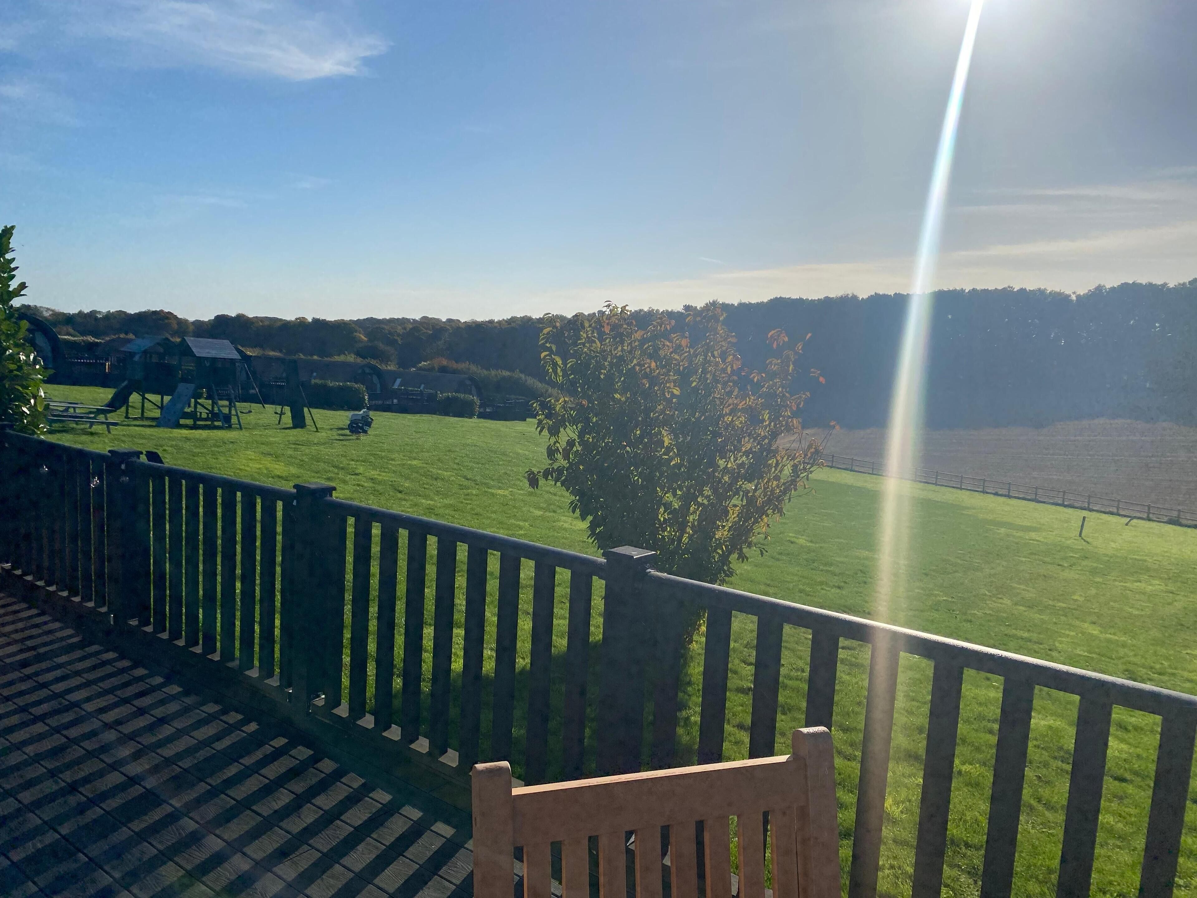 A wooden deck with a bench, overlooking a grassy field with playground equipment and a tree.