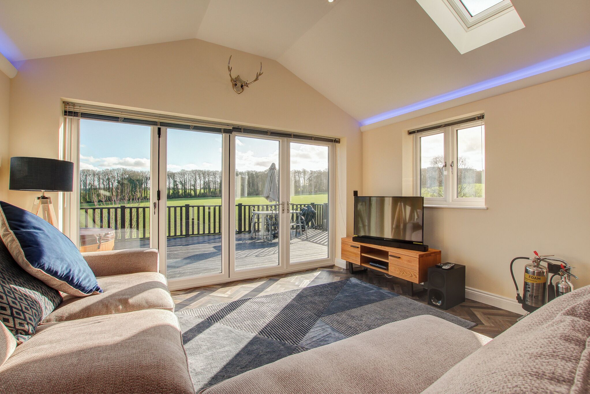 A spacious living room with a large sliding glass door leading to a balcony, a flat-screen TV, a fireplace, and a ceiling skylight.
