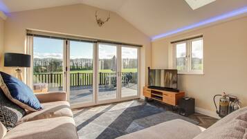 A spacious living room with a large sliding glass door leading to a balcony, a flat-screen TV, a fireplace, and a ceiling skylight.