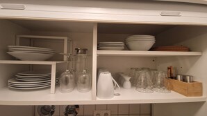 A kitchen shelf with white plates, bowls, wine glasses, and jars. - Cozy 1-room apartment in the Hildesheim forest (Diekholzen)
