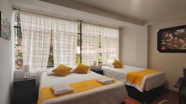 Une chambre d’hôtel avec deux lits, du linge de lit blanc, des coussins décoratifs jaunes, une petite table avec une lampe et un tableau au mur.