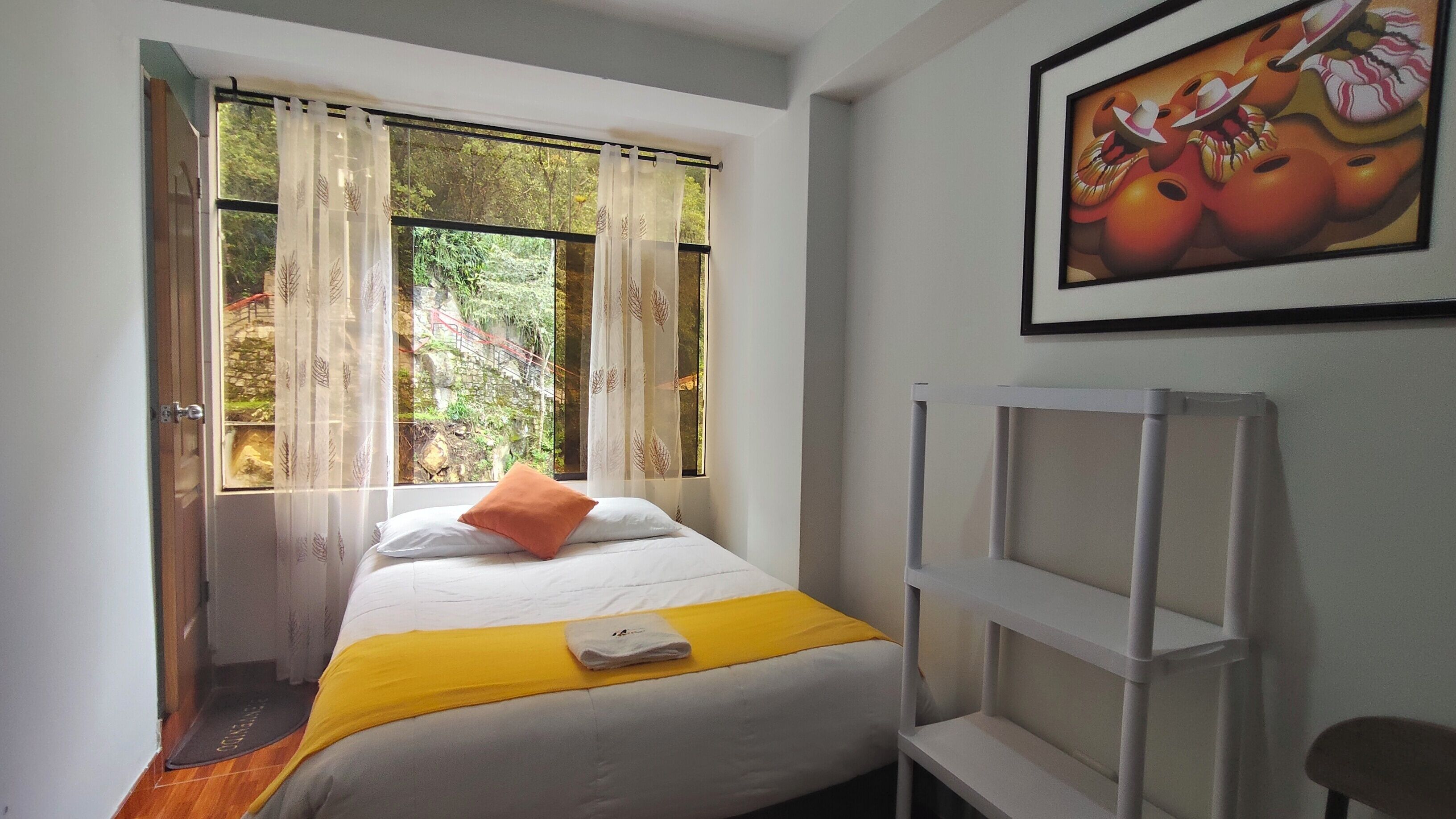 A bedroom with a bed, a yellow throw, a white pillow, a white shelf, and a painting on the wall.