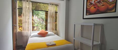 A bedroom with a bed, a yellow throw, a white pillow, a white shelf, and a painting on the wall.