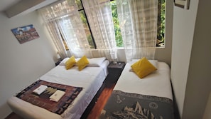 A room with two beds, each with white bedding and yellow pillows, a small table with a lamp, and a painting on the wall. - B & B VERONICA (Aguas Calientes)