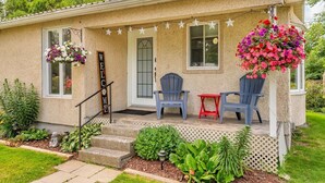 Ein Haus mit Veranda, zwei blaue Stühle, einem roten Tisch und hängenden Blumenkörben.