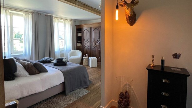 Ein Schlafzimmer mit Bett, Kommode, einem Hirschgeweih an der Wand und einem Fenster mit Vorhängen.