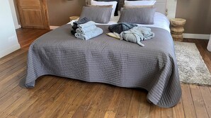 Ein ordentlich bezogenes Bett mit grauer Bettwäsche, Holzboden und einem Bild an der Wand.