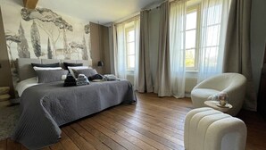 Ein Schlafzimmer mit einem großen Bett, einem Sessel und einem kleinen Tisch mit einem Glas und einem dekorativen Gegenstand.