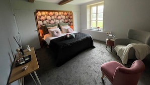 Une chambre avec un grand lit, une petite table avec une lampe, une chaise et une fenêtre donnant sur un paysage verdoyant.