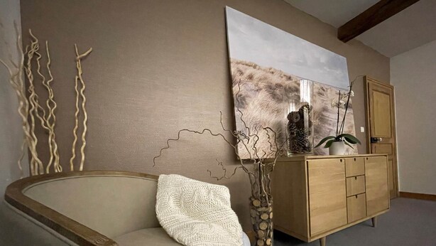 Ein Wohnzimmer mit einem beigefarbenen Sofa, einer weißen Strickdecke, einem Holzschrank und einem großen abstrakten Gemälde an der Wand.