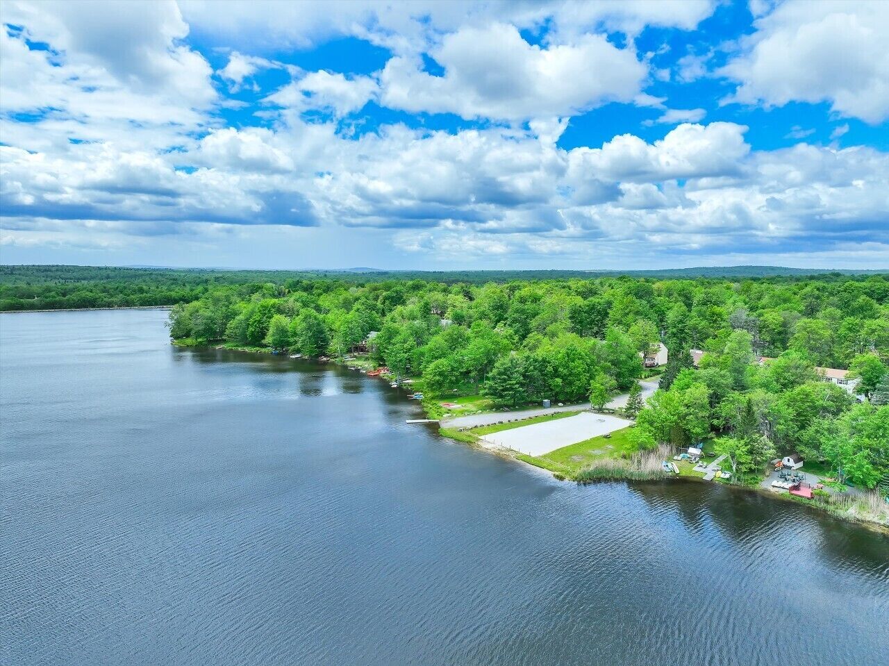 An aerial view of a lakeside property with a dock, a grassy area, and a row of cabins.