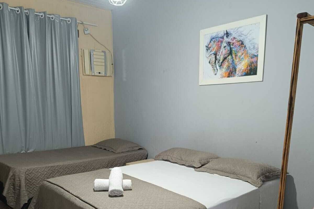 Ein Zimmer mit zwei Betten, einem Holzstuhl, einem Bild an der Wand und einer Deckenleuchte.