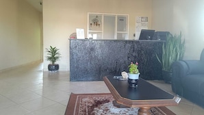 Un espace d’accueil avec un comptoir en marbre, une plante en pot, une petite table avec un vase et un canapé noir.