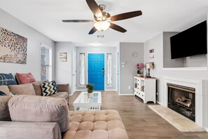A living room with a beige sofa, a coffee table, a ceiling fan, a blue door, and a fireplace. - Quiet Austin Stay Near Tech (Austin)