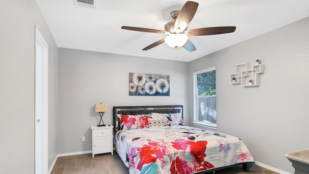 A bedroom with a bed, a nightstand, a ceiling fan, a window, and a wall with a painting. - Quiet Austin Stay Near Tech (Austin)