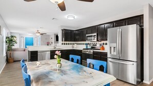 A modern kitchen with dark cabinets, stainless steel appliances, and a marble dining table with blue chairs. - Quiet Austin Stay Near Tech (Austin)