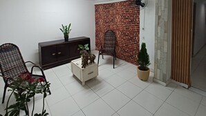 Un salon avec un mur en briques, un fauteuil noir, un meuble blanc et une petite table ornée de plantes.