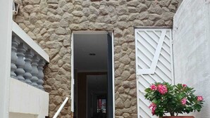 Un escalier menant à une porte, avec un mur en pierre, une plante en pot et une rambarde blanche.