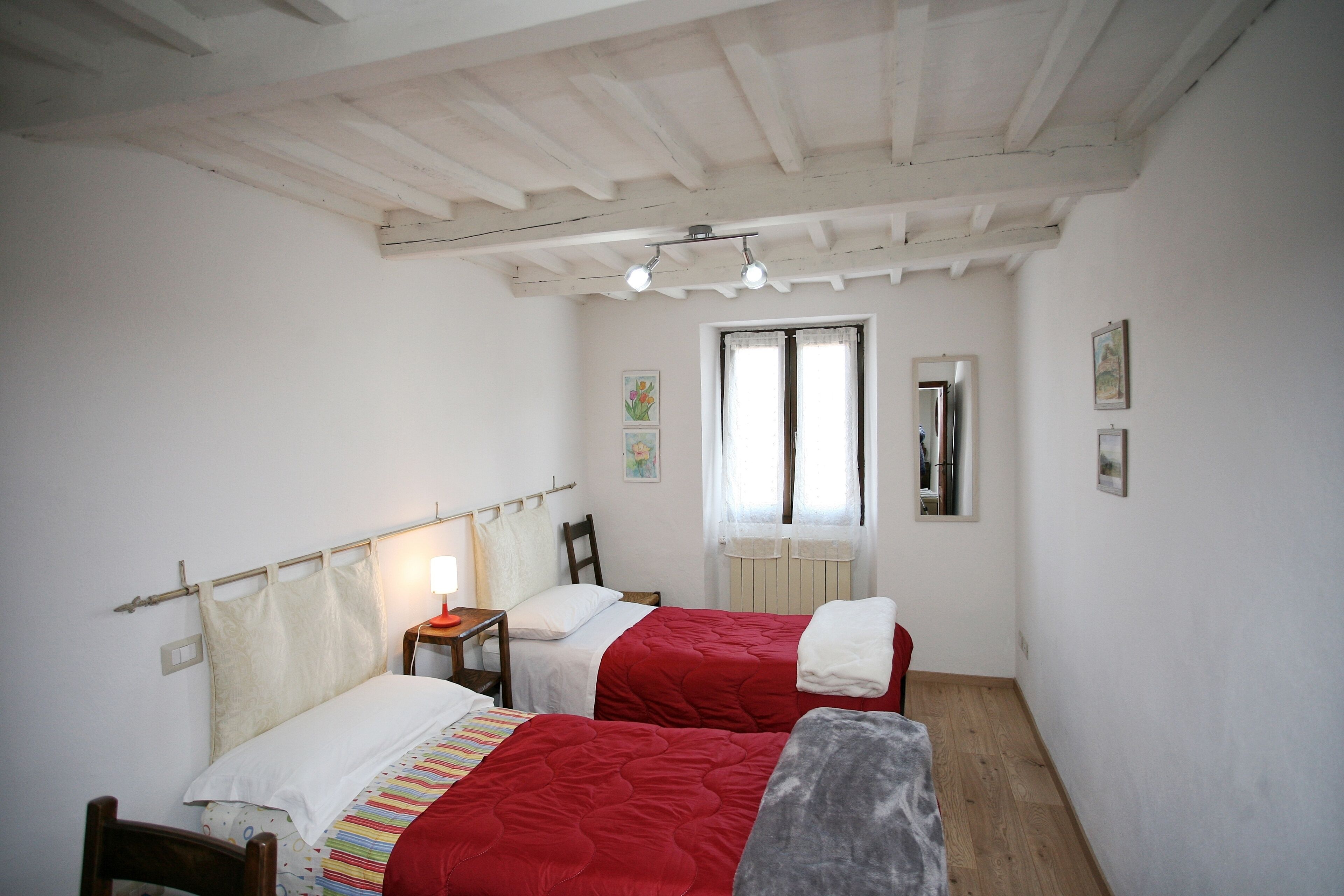 Quarto com duas camas, uma cadeira de madeira, uma escrivaninha e uma janela com cortinas.