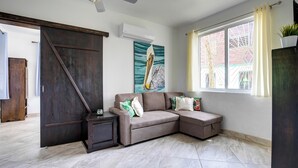 Una sala de estar con un sofá modular, un ventilador de techo, un ventanal con cortinas y un cuadro en la pared.