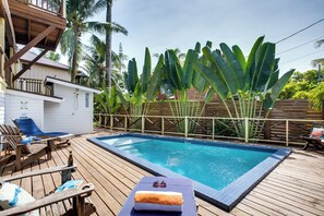Eine Holzterrasse mit Schwimmbecken, Liegestühlen und einem kleinen Gebäude mit Balkon.